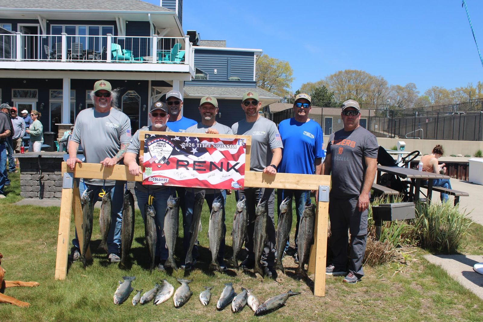 A group of veterans with their salmon catch beside a RENK sponsor banner and a wooden display frame