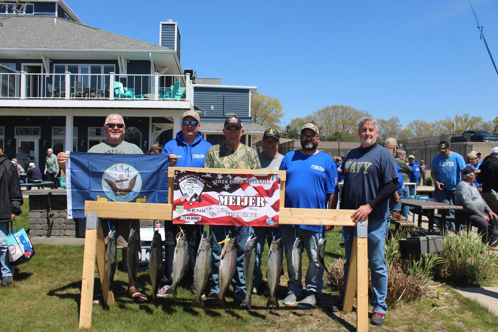 Event participants displaying their salmon haul with sponsor banners at the lakeside venue