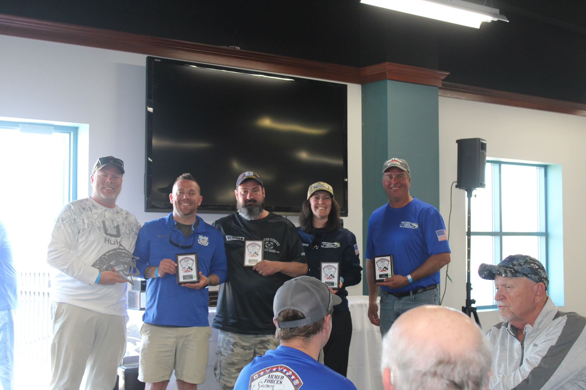 Armed Forces Salmon Assault team members display award bottles and merchandise while posing for a group photo at what appears to be a community event or fundraiser.