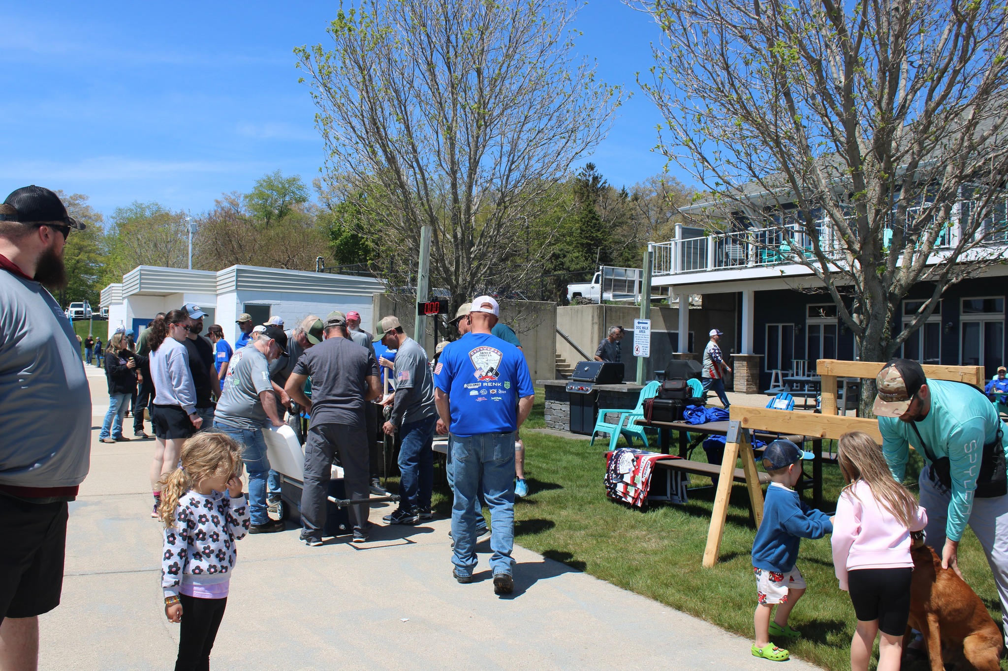 A community gathering at Armed Forces Salmon Assault featuring outdoor food service, picnic seating, and families enjoying a sunny spring event.