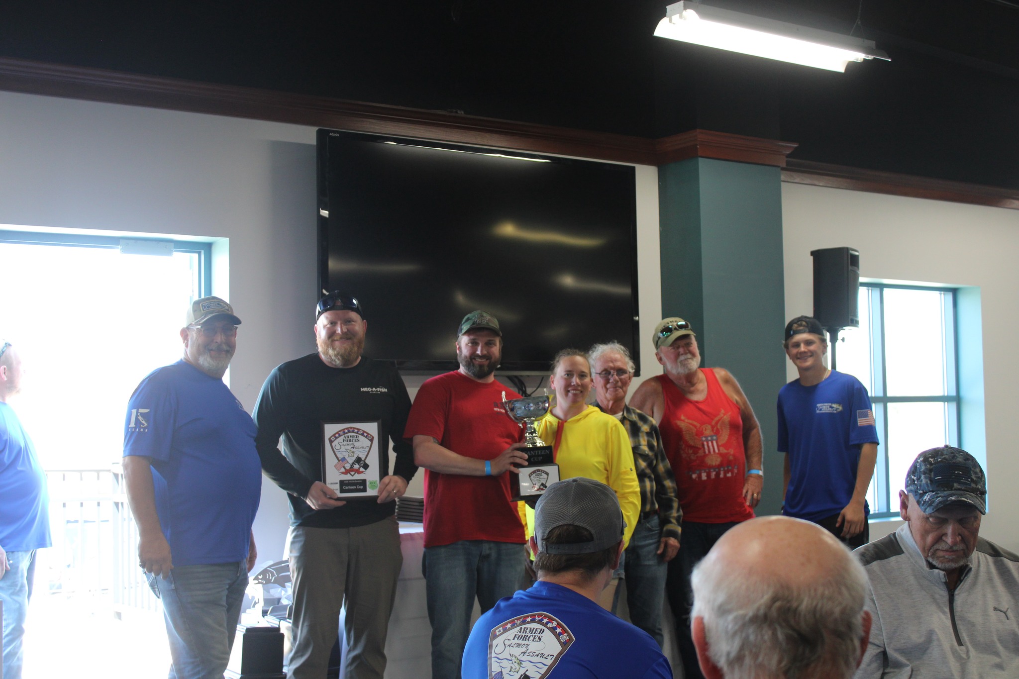 A group of people posing indoors at what appears to be a community event or gathering, with individuals holding a trophy.