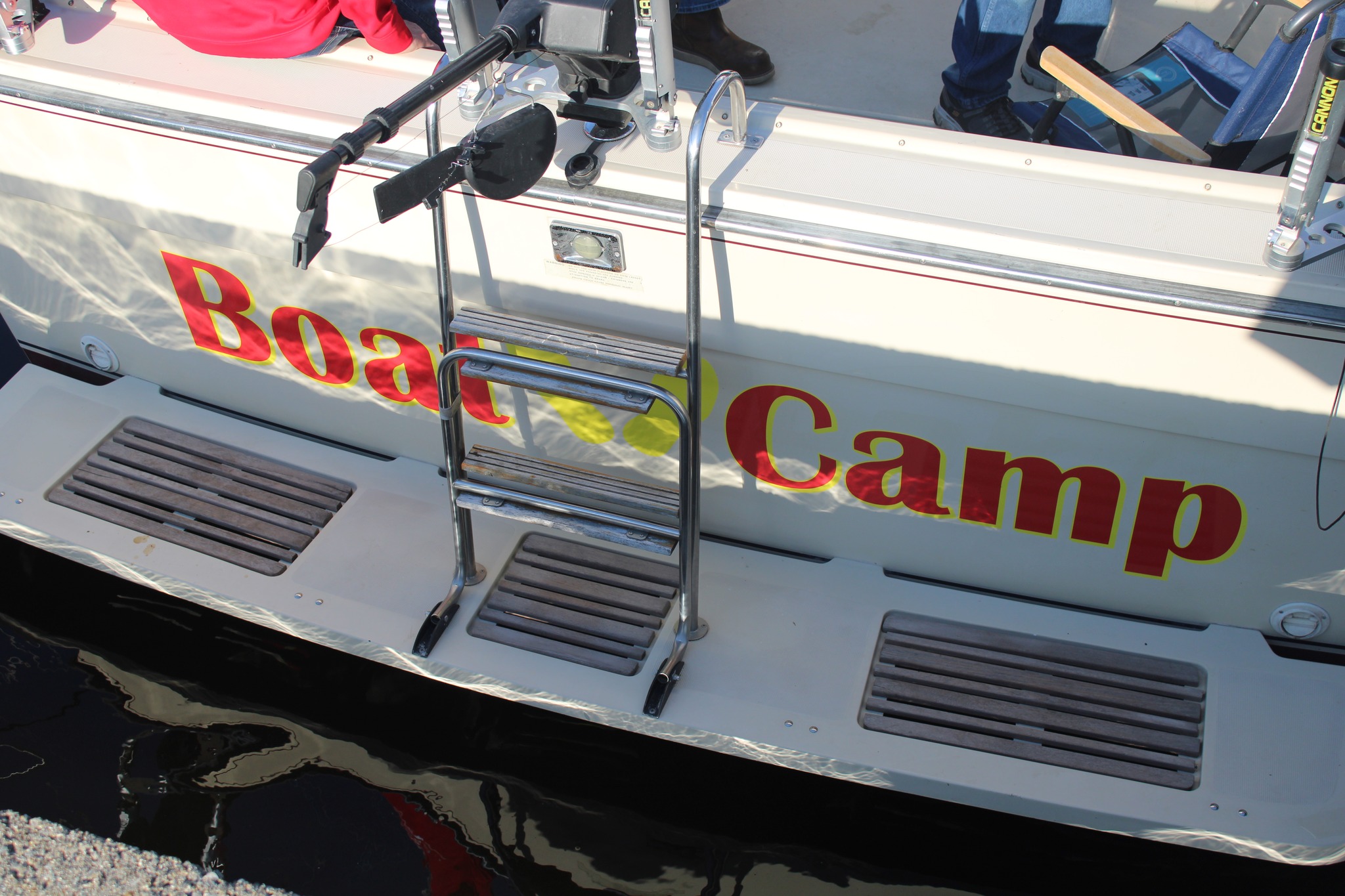 The side of a white boat with red and yellow lettering reading "Boat Camp," displaying the business name and branding on the vessel's hull.
